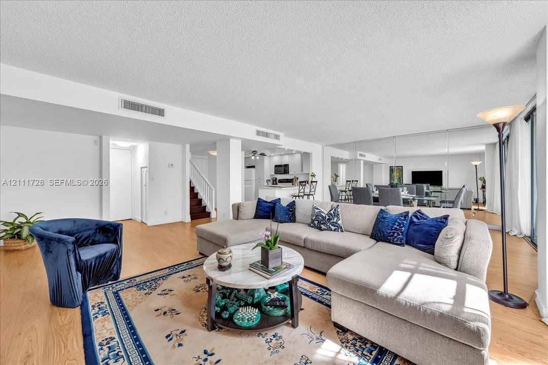 Open-concept interior featuring wood-finish flooring, full-wall mirrored accents, recessed ceiling lighting, and a staircase with a wooden handrail