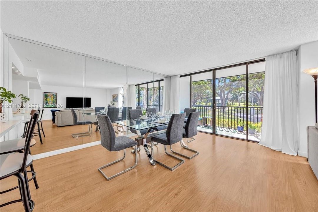 Open-concept living space featuring wood-finish flooring, full-wall mirrored accent, and floor-to-ceiling sliding glass doors opening to a balcony