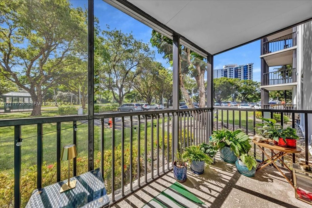 Screened-in balcony featuring metal railings, concrete flooring, and mature tree-lined landscaping