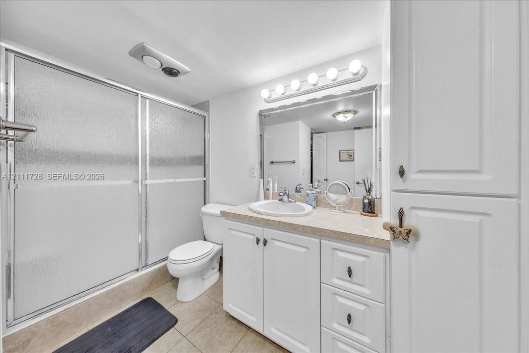 Bathroom featuring a vanity with white cabinetry and a solid-surface countertop, an integrated sink with a chrome faucet, a shower enclosure with frosted sliding doors, and built-in floor-to-ceiling storage cabinetry