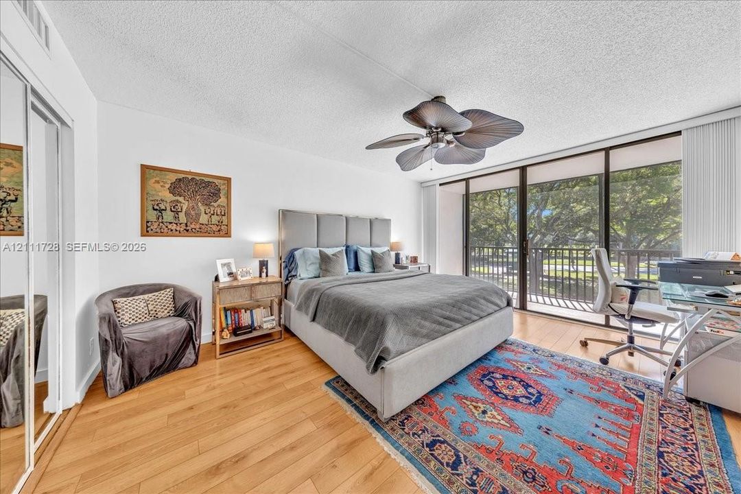 Wood-finish flooring, floor-to-ceiling glass sliding doors, private balcony, mirrored closet doors, and leaf-blade ceiling fan