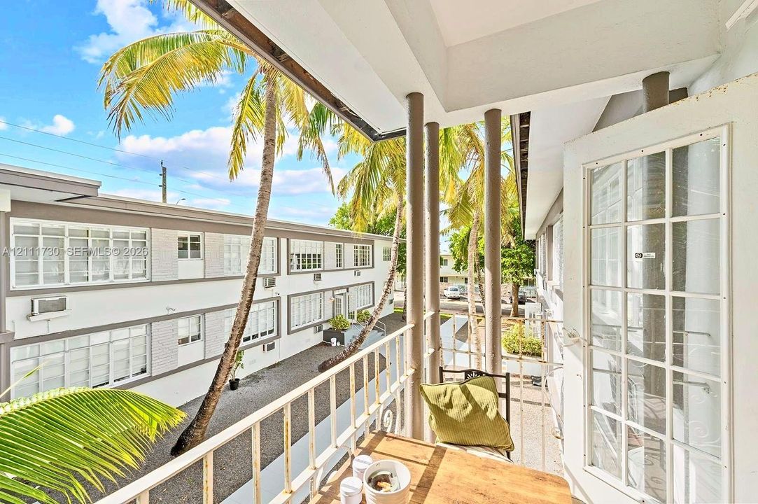 Covered balcony featuring white metal railings, cylindrical support columns, and multi-pane glass door entry