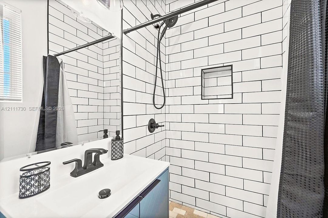 Bathroom featuring a white subway-tile shower surround with contrasting dark grout, a recessed wall niche, matte black fixtures, and a modern vanity with a rectangular basin