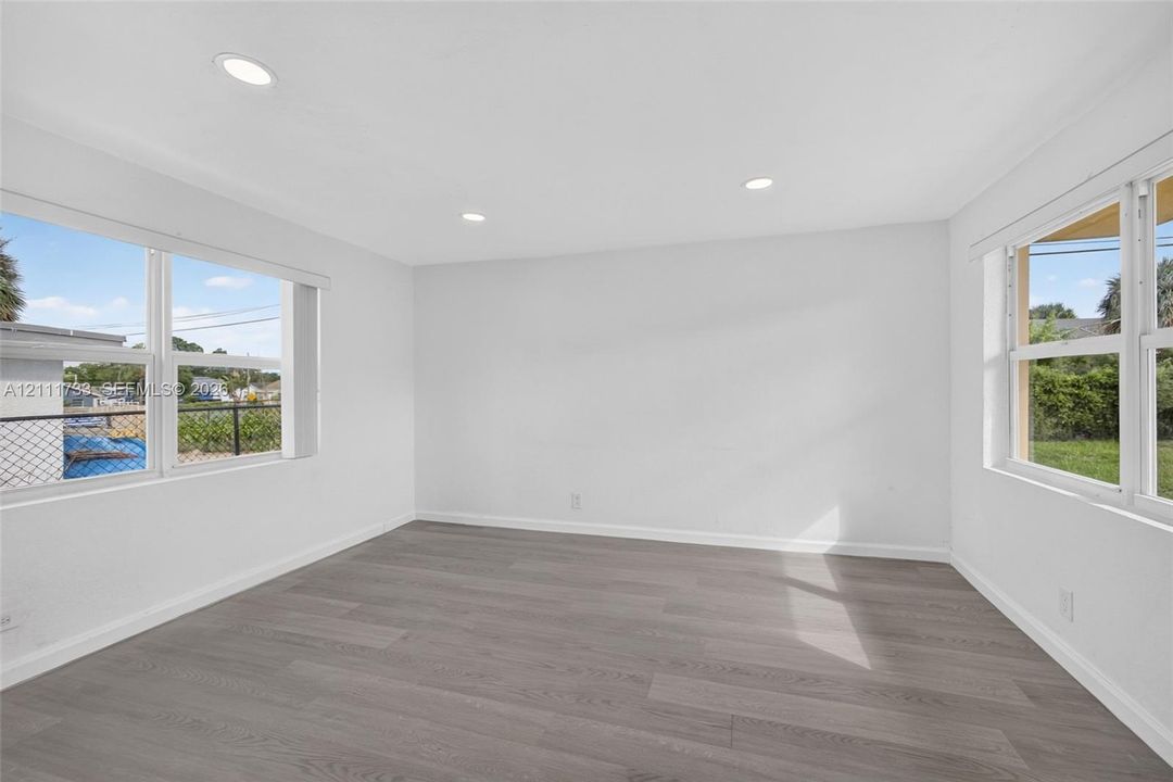 Rear bedroom features Neutral-toned wood-finish flooring, recessed lighting, and multiple large windows with white trim