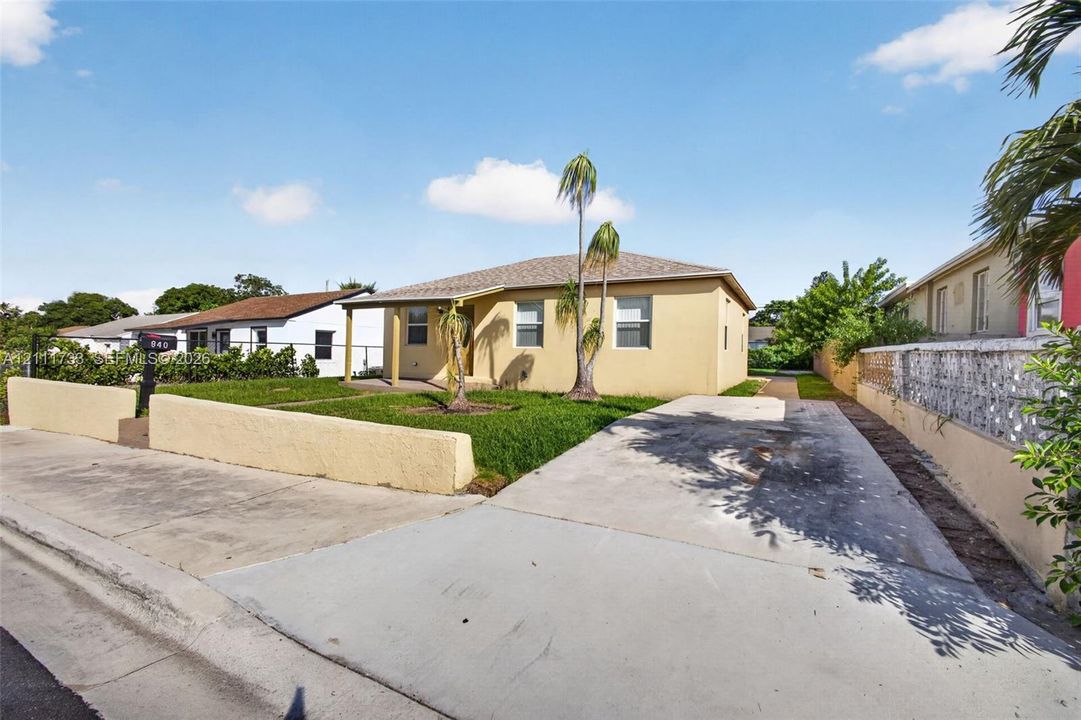 Exterior featuring a stucco facade, hipped roof, two Palm Trees, concrete driveway, and front lawn enclosed by a masonry wall.