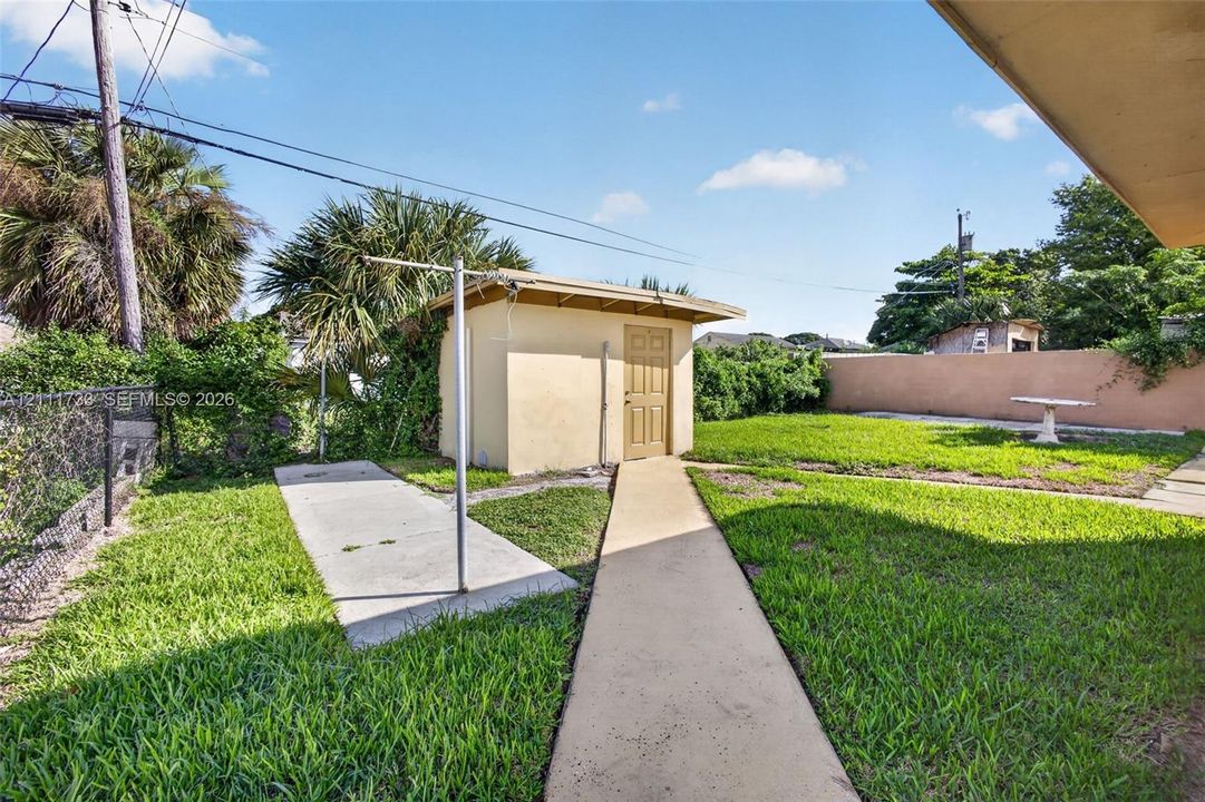 Rear yard from left side of home, featuring a detached shed with  laundry room, concrete pathways, perimeter masonry wall.