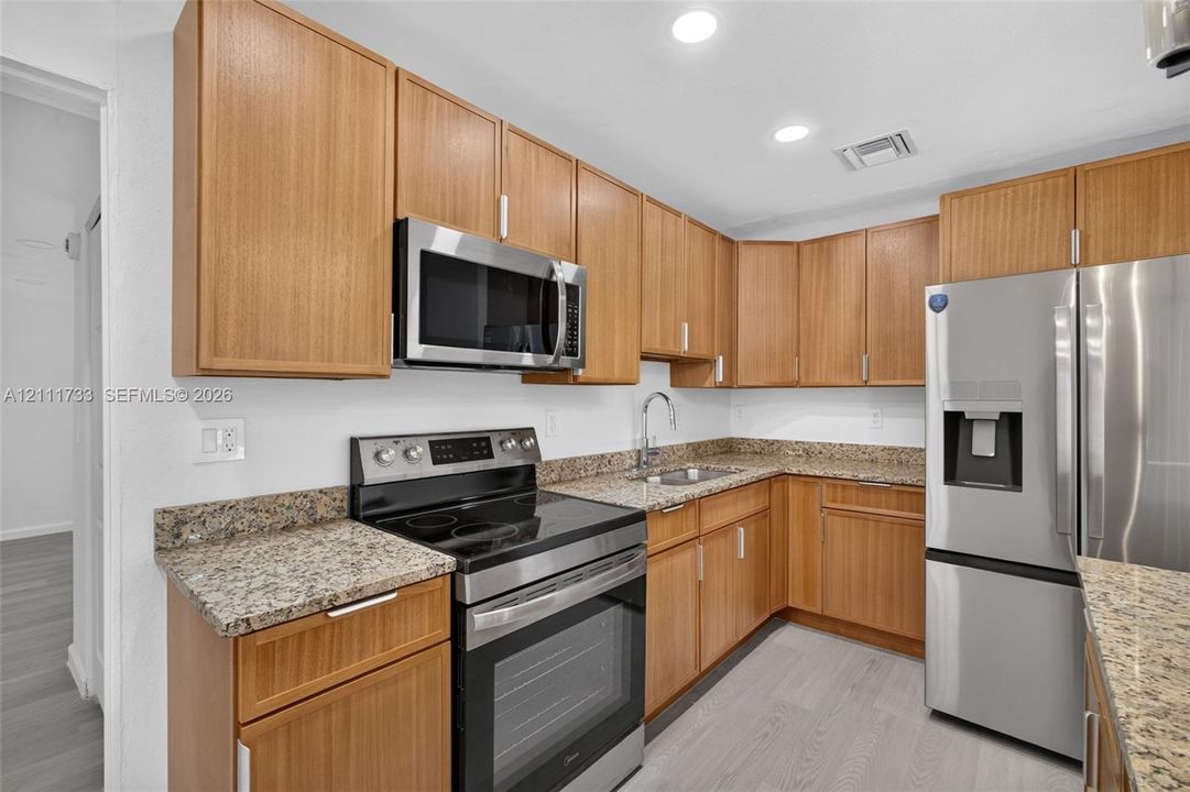 Kitchen featuring wood cabinetry, stone-finish countertops, stainless steel appliances, and wood-finish flooring