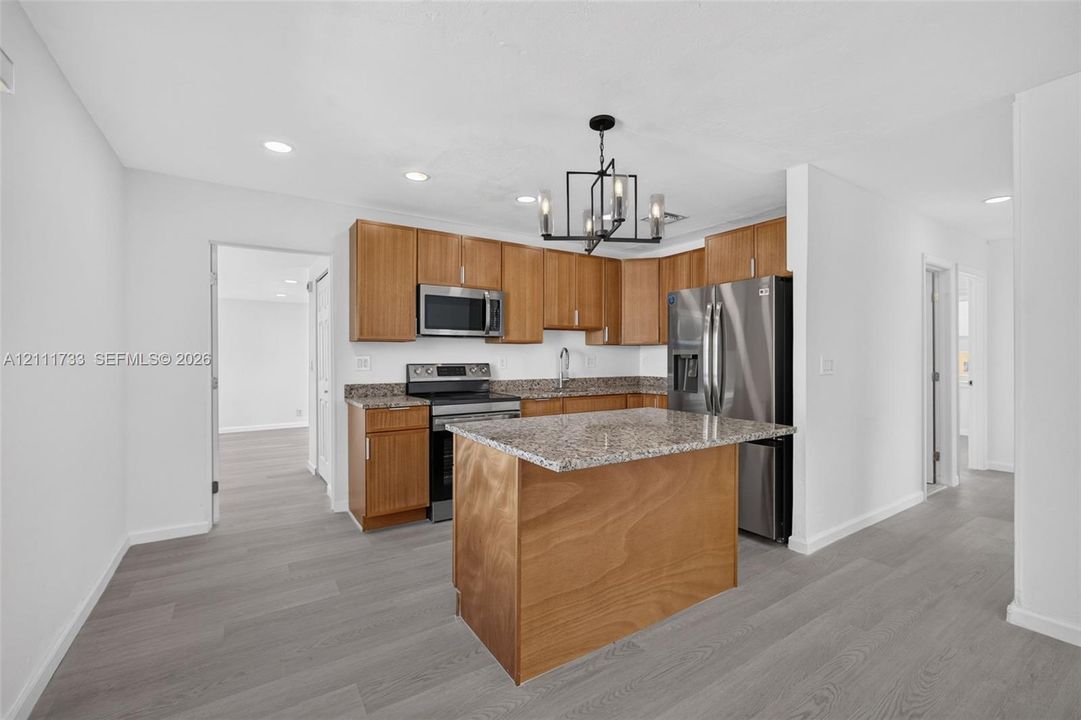 Kitchen featuring natural wood cabinetry, stone-surface countertops, stainless steel appliances, a central island, and a geometric chandelier