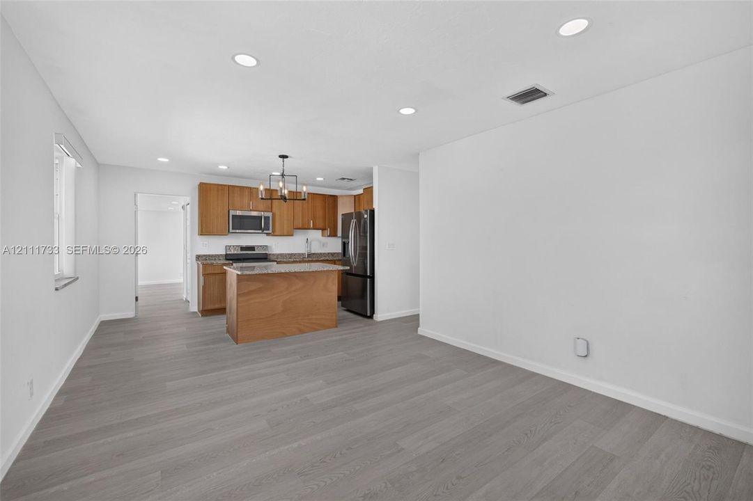 Kitchen featuring wood-finish cabinetry, an island, stone-surface countertops, stainless steel appliances, and recessed ceiling lighting throughout