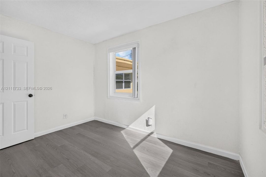 Neutral-toned wood-finish flooring, single-panel interior door, and a white-framed window