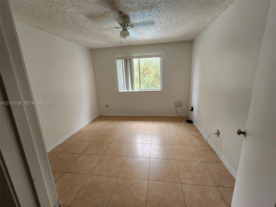 Neutral-toned room featuring large-format square tile flooring, a textured ceiling, a central ceiling fan, and a single window with vertical blinds