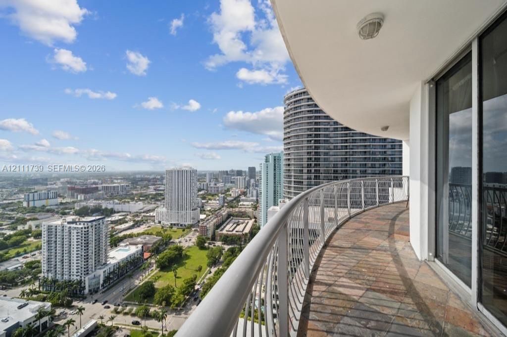 Curved exterior balcony with stone tile flooring, metal railing, and sliding glass doors
