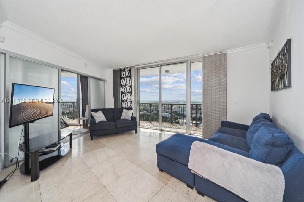 Living area featuring large-format light tile flooring, expansive glass sliding doors, and a balcony with metal railings