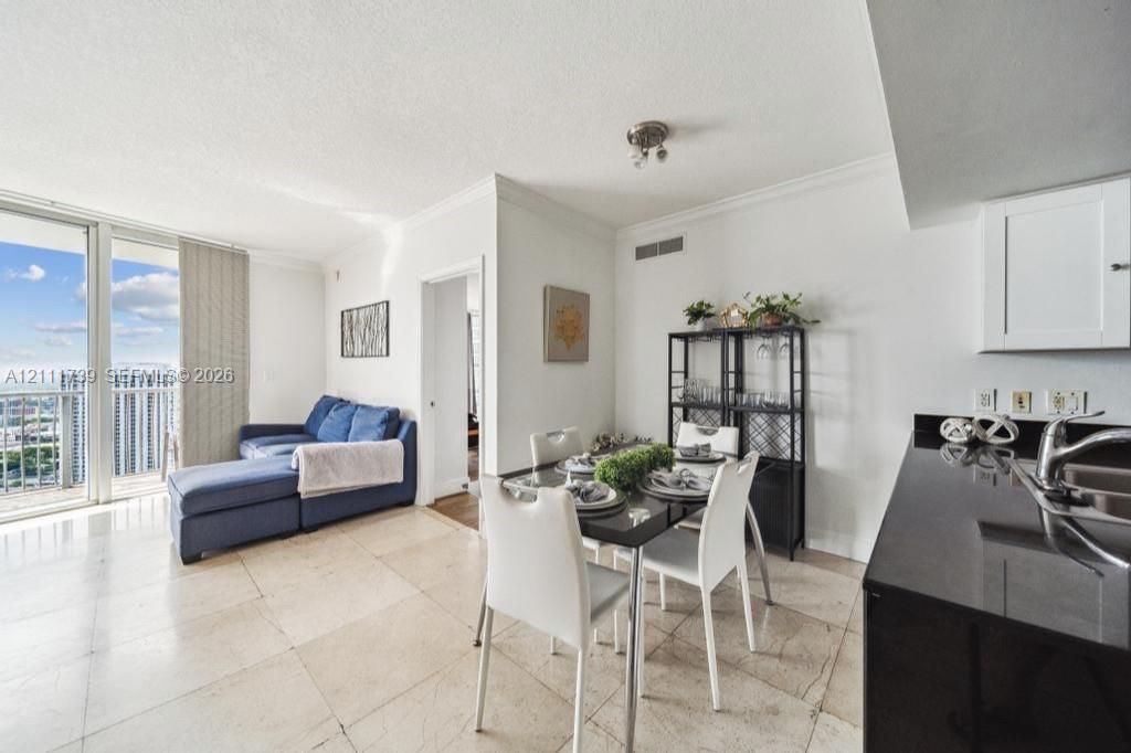 Open-concept interior featuring large-format tile flooring, floor-to-ceiling glass sliding doors, and kitchen area with dark stone countertops and white cabinetry