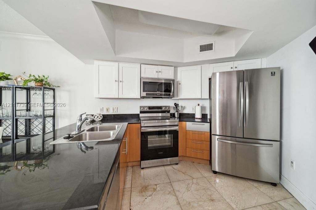Kitchen featuring white upper cabinetry, wood-finish lower cabinets, dark stone countertops, stainless steel appliances, and tile flooring