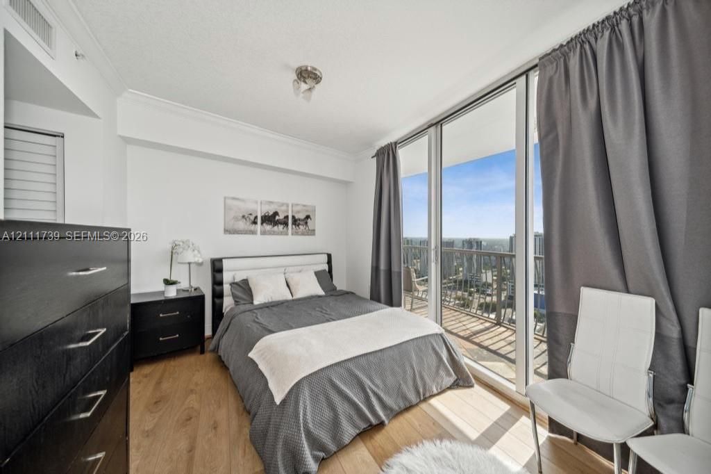 Floor-to-ceiling glass sliding doors, wood-finish flooring, and an attached balcony with metal railings