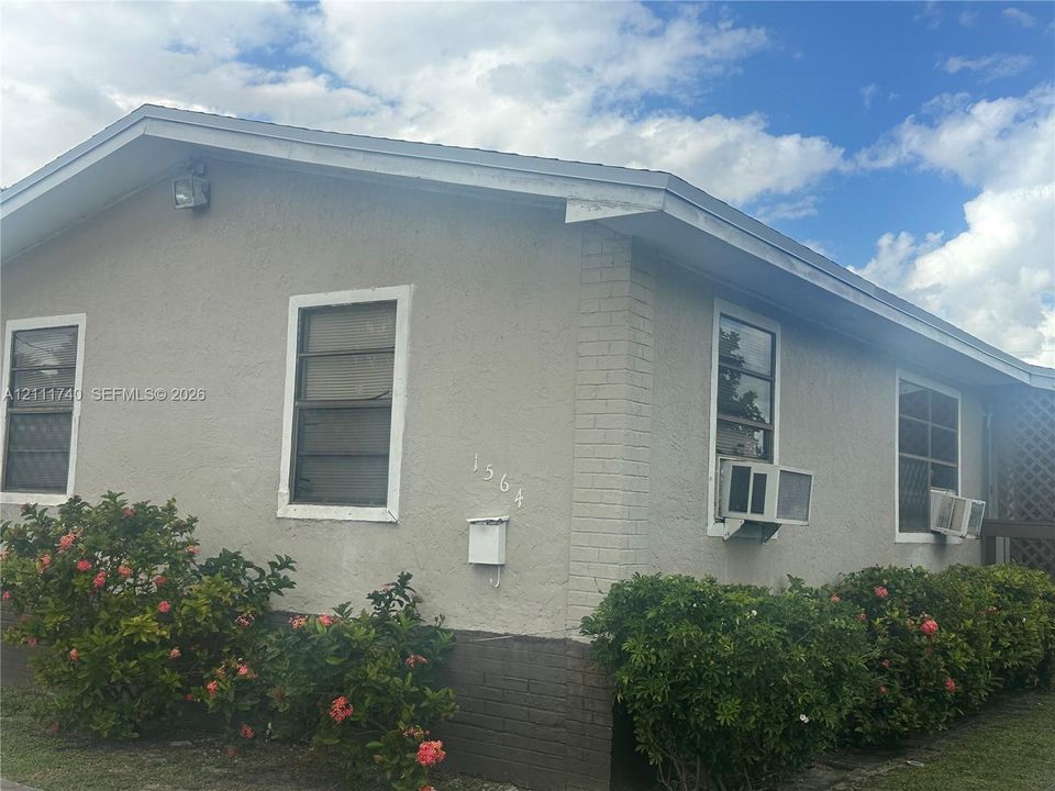 Stucco exterior featuring brick corner detailing, metal-framed windows, and foundation-level decorative masonry