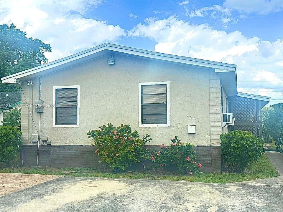 Exterior facade featuring a stucco finish, brick base, two single-hung windows, and a paved driveway