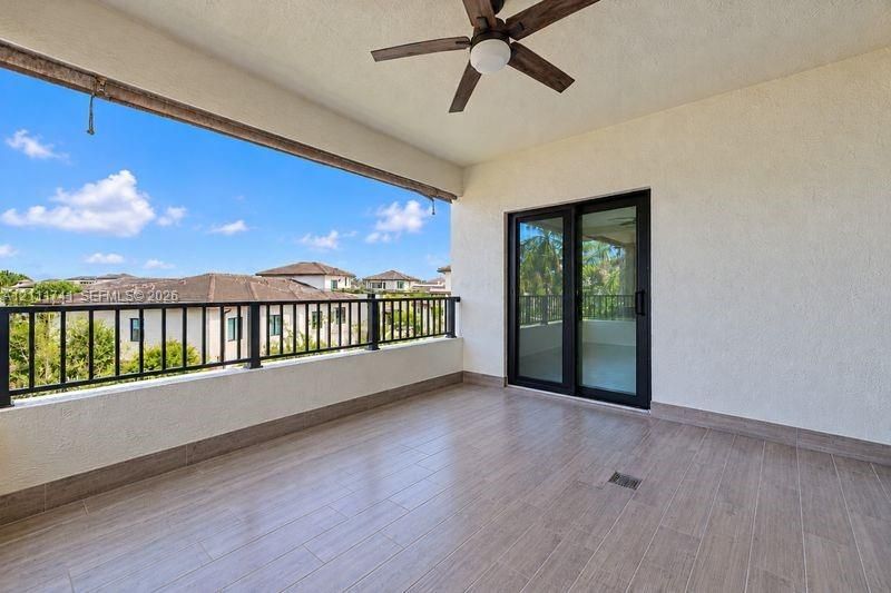 Covered balcony featuring wood-finish tile flooring, a black metal railing, a ceiling fan, and sliding glass entry doors