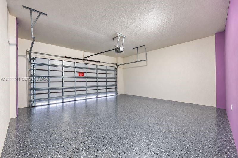 Two-car garage featuring epoxy-coated flooring, an automated overhead door system, and high-clearance ceilings