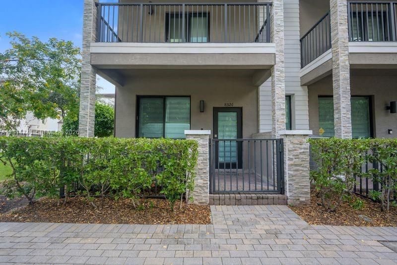 Multi-story exterior featuring stone veneer accents, a gated private entrance, paver walkway, and an upper-level balcony with metal railing