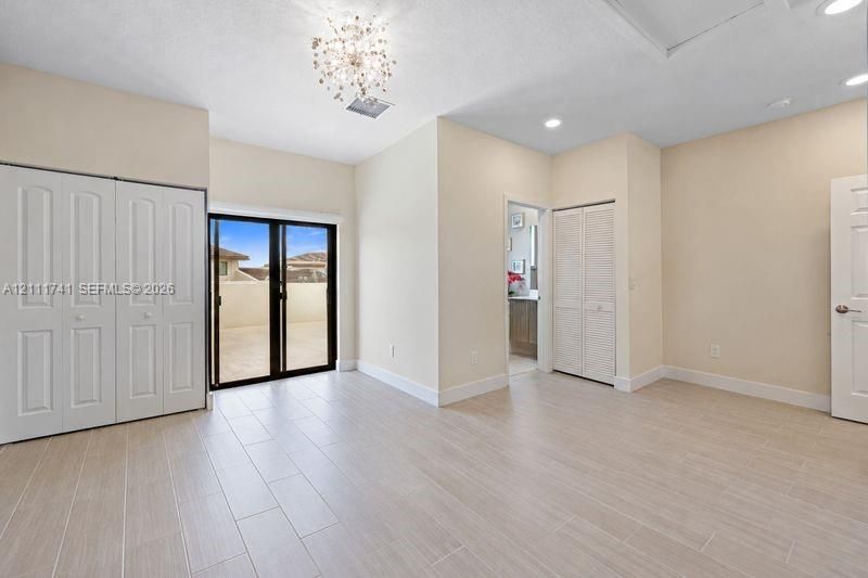 Spacious room featuring neutral tile flooring, a decorative crystal-style chandelier, recessed lighting, double-door closet storage, and sliding glass doors with access to an exterior terrace