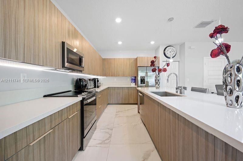 Contemporary kitchen featuring wood-grain flat-panel cabinetry, white quartz countertops, integrated under-cabinet lighting, large-format tile flooring, and a stainless steel appliance suite