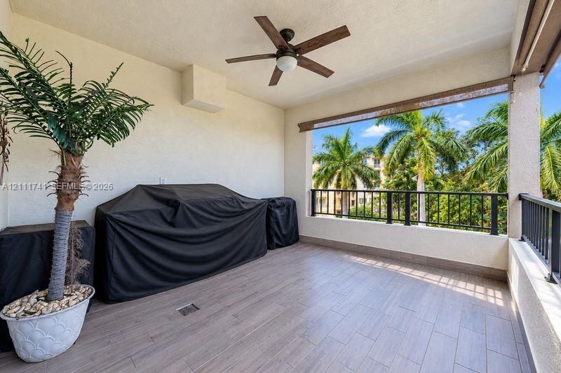 Covered balcony featuring wood-finish flooring, a ceiling fan, and metal railings