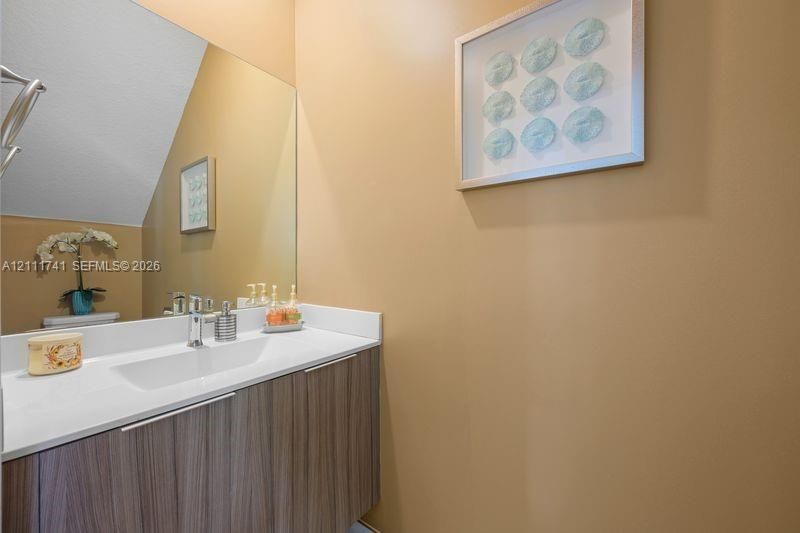Wall-mounted vanity featuring wood-finish cabinetry, a white countertop with an integrated rectangular sink, a polished chrome faucet, and a large plate-glass mirror
