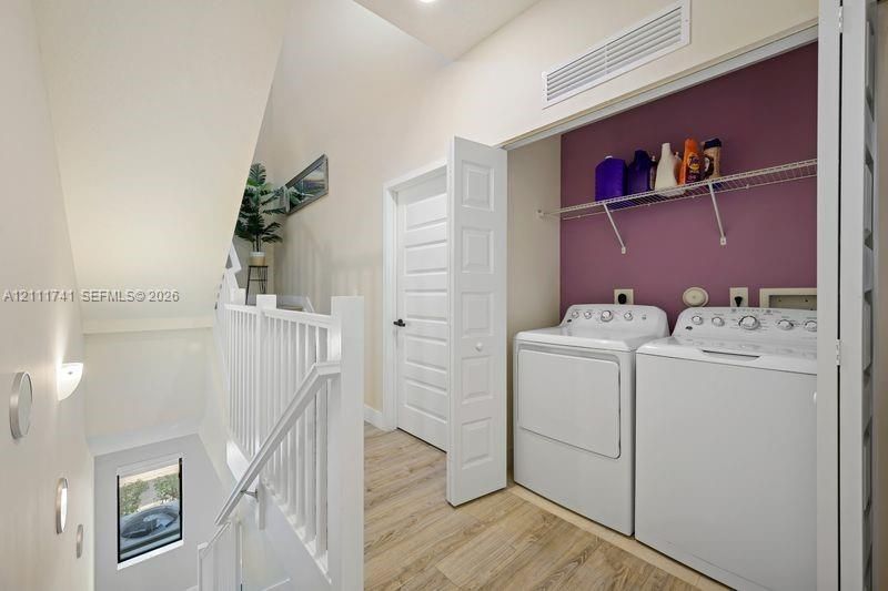 Laundry area featuring built-in wire shelving, white panel door, and wood-finish flooring, accompanied by a white wooden handrail and balusters