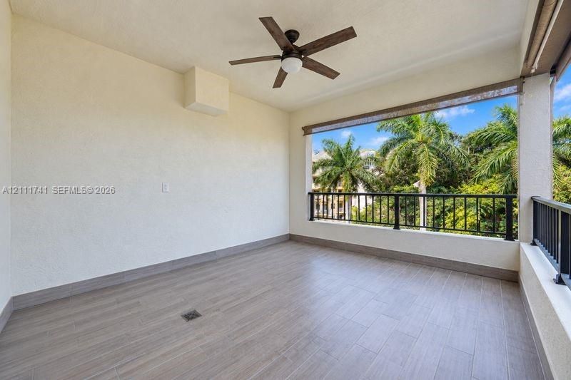 Covered balcony featuring wood-finish tile flooring, matte black metal railings, a ceiling fan with integrated lighting, and roll-down shades