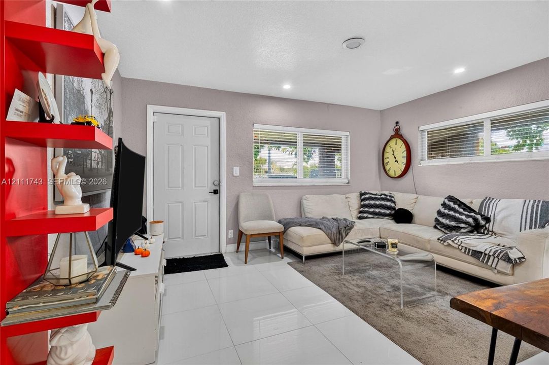 Bright living area featuring glossy large-format floor tiles, recessed lighting, double-pane windows, and a built-in floor-to-ceiling shelving unit