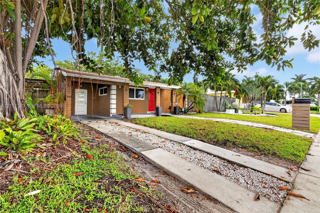 Single-story exterior featuring a brown stucco facade, brick-accented columns, a paved concrete driveway with aggregate detailing, and mature perimeter landscaping