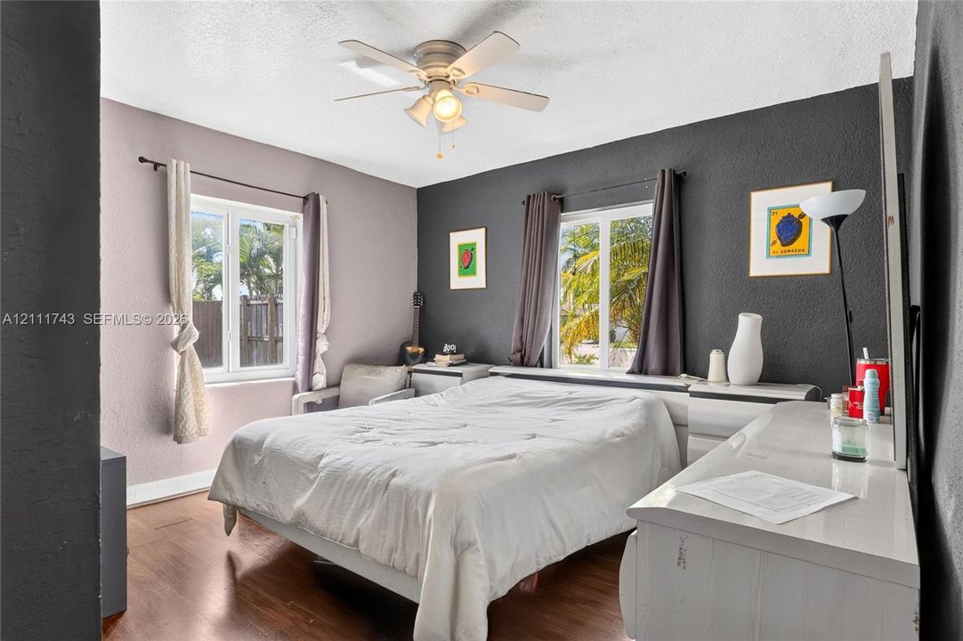 Wood-finish flooring, dual windows with deep-set frames, and a ceiling-mounted light fixture with a multi-blade fan