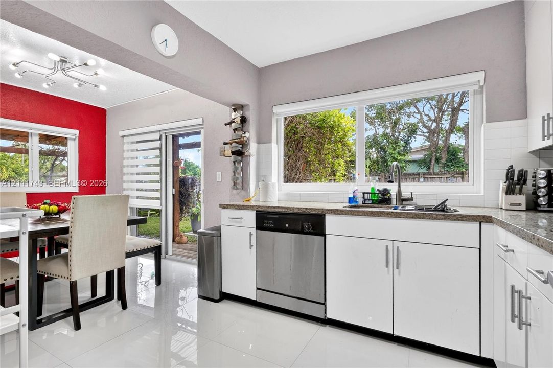 Kitchen featuring white cabinetry, stone-finish countertops, large-format tile flooring, a stainless steel dishwasher, and a multi-arm modern ceiling light fixture