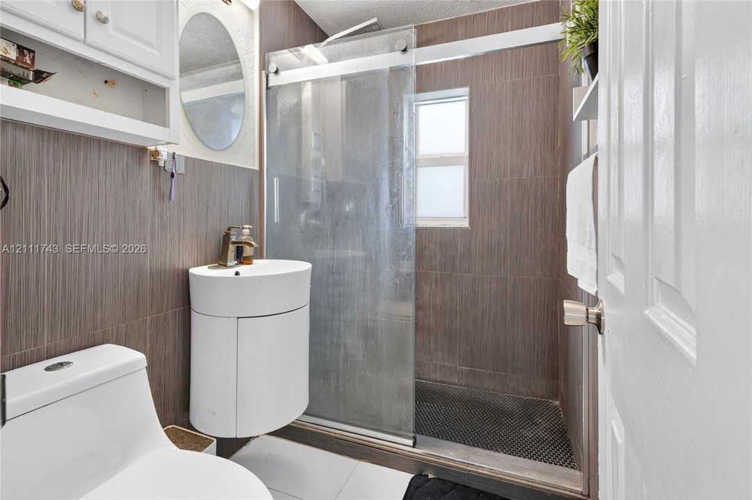 Bathroom featuring vertical wood-finish wall tile, a semi-circular pedestal sink with a metallic faucet, and a shower enclosure with a glass sliding door