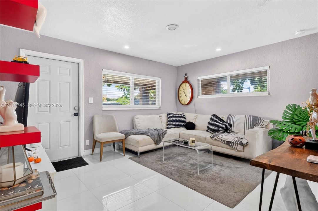 Interior space featuring large-format tile flooring, recessed ceiling lighting, dual windows with horizontal blinds, and a solid-core entry door