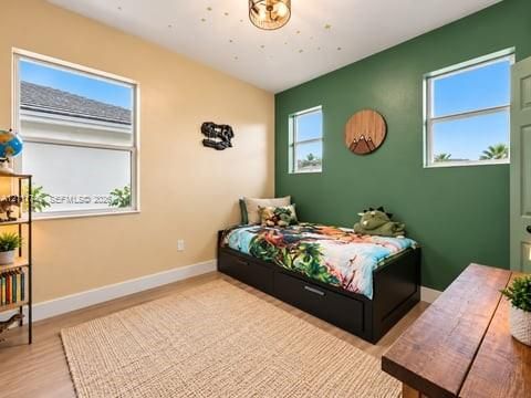 Bedroom featuring wood-finish flooring, dual-tone painted walls, three double-pane windows, and a circular flush-mount ceiling light
