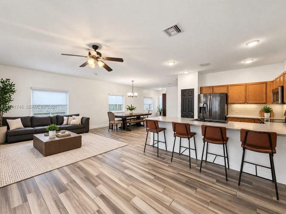 Open-concept interior featuring wood-finish flooring, a kitchen island with stone-surface countertop, wood cabinetry, recessed lighting, and a ceiling fan