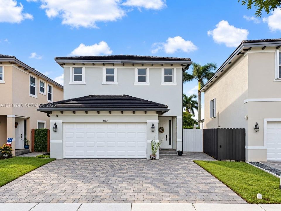 Two-story exterior featuring a light-toned stucco facade, a dark tile roof with extended eaves, a paver driveway, and a two-car garage