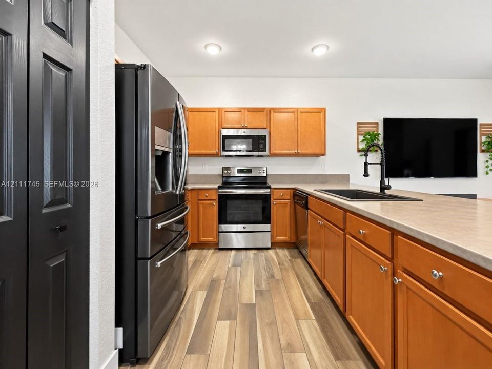 Kitchen featuring wood-finish cabinetry, stainless steel appliances, a black drop-in sink with a high-arch matte black faucet, solid-surface countertops, and wood-finish flooring