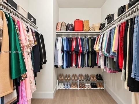 Walk-in closet featuring tiered wire shelving, supplemental upper shelf storage, and wood-finish flooring