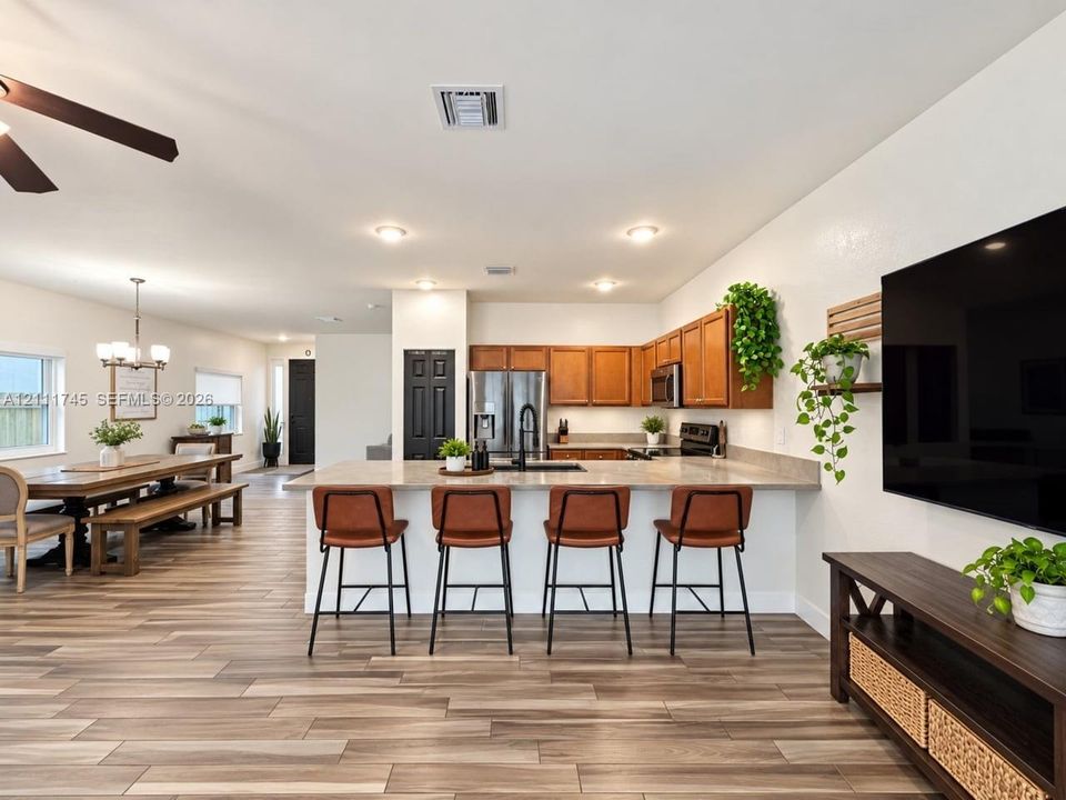 Open-concept kitchen featuring wood-finish cabinetry, stone-surface countertops, a breakfast bar, and wood-finish flooring throughout