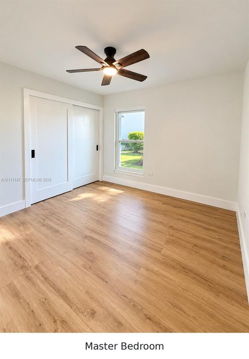 Wood-finish flooring, sliding closet doors with matte black hardware, and a ceiling-mounted light fixture with a multi-blade fan