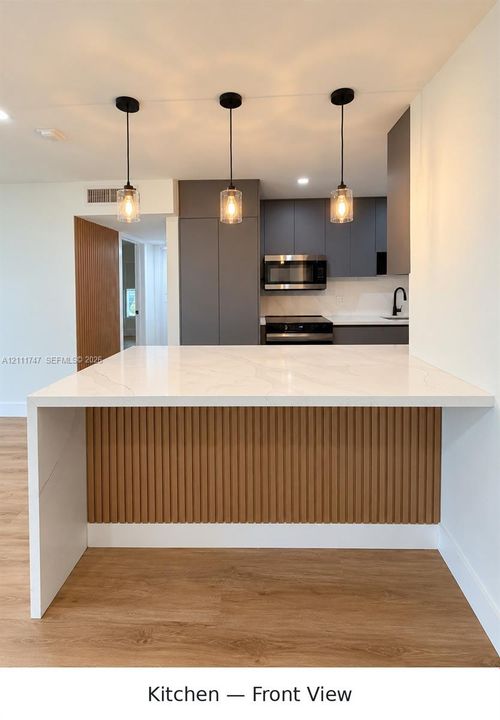 Kitchen featuring a waterfall island with a slatted wood base, flat-panel cabinetry, quartz countertops, three pendant lights, and stainless steel appliances