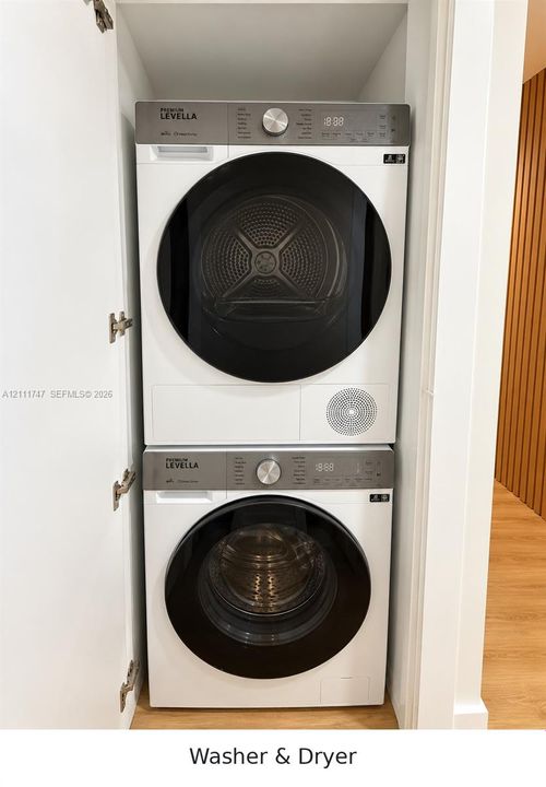 Stacked laundry center featuring a front-load washer and dryer with digital control panels, high-contrast black glass circular doors, and a space-saving recessed cabinetry enclosure