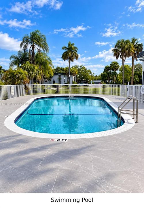 In-ground swimming pool featuring a tile border, metal handrail, white perimeter fencing, and stone-finish decking