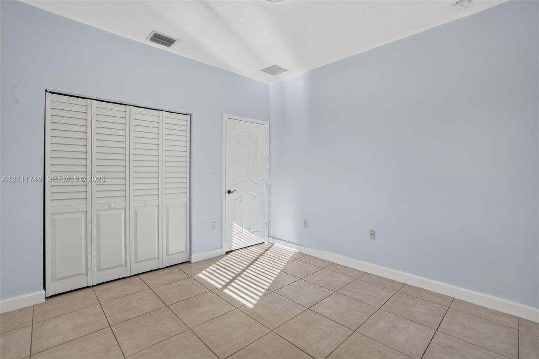 Neutral-toned interior featuring ceramic tile flooring, a four-panel closet with white louvered doors, and a six-panel door with brushed nickel hardware