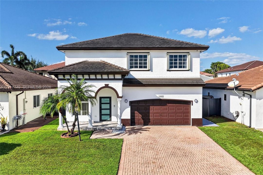 Two-story stucco exterior featuring a tiled roof, covered entryway with arched columns, multi-pane windows, and a brick-paver driveway leading to an attached two-car garage
