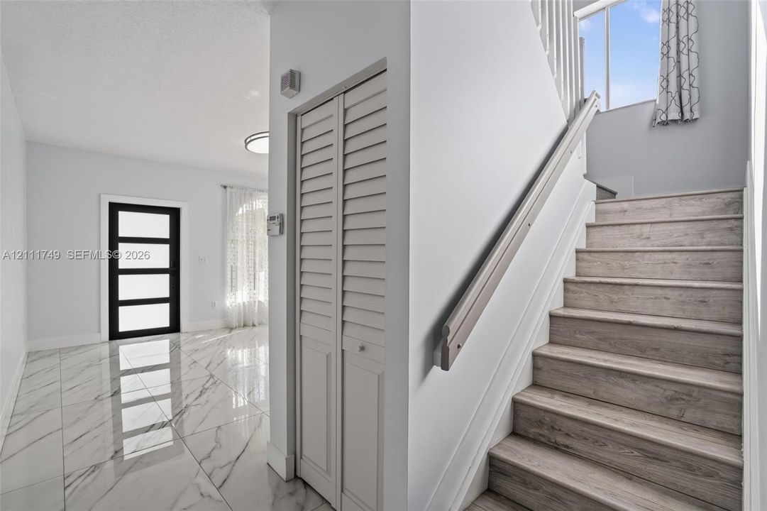 Foyer featuring large-format tile flooring with a marble-style finish, staircase with wood-finish treads, louvered bi-fold closet doors, and an exterior door with horizontal glass panels